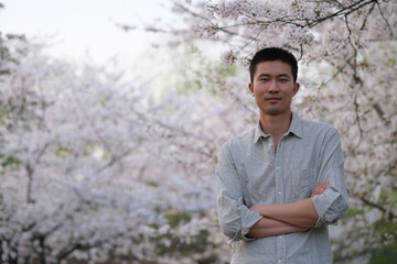 mid shot of one Asian young man under white sakura flower tree, looking at camera 