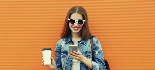 Portrait close up of smiling young woman with smartphone wearing a denim jacket on an orange background