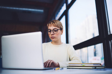 Pensive female freelancer using laptop in workspace