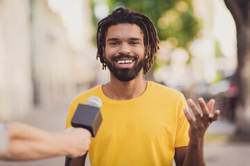 Photo portrait of young man smiling giving interview to journalist talking in microphone on street - obrazy, fototapety, plakaty