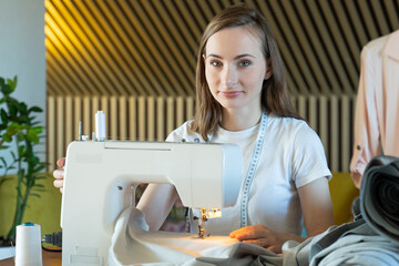 Young woman seamstress sews on a sewing machine sitting at a table