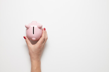 Person hand holding pig piggy bank with money on grey background with copy space. Top view, flat lay © Shi 