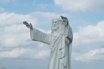 Jesus statue standing and blessing with both the hands against blue sky background.