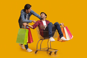 Two young men talking with one of them sitting in a trolley holding carry bags.	