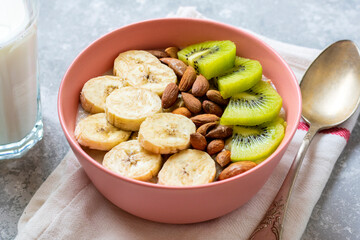 oatmeal with banana, almonds nuts and kiwi slices in pink bowl, glass of milk, napkin on gray concrete background Top view Healthy breakfast or lunch Natural ingredients Rustic style