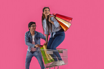 A young man moving a trolley with a woman holding carry bags standing  in it.	