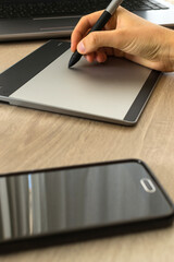 Person using graphic tablet connected to his laptop. Next to it, a smartphone. Graphic designer, photographer or digital artist tools.