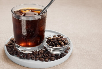Iced coffee in a low glass with ice and a straw on a white plate on a beige background. Copy space