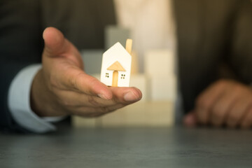 Realtors in suit holding mini wood house model. The concept of selling a home.