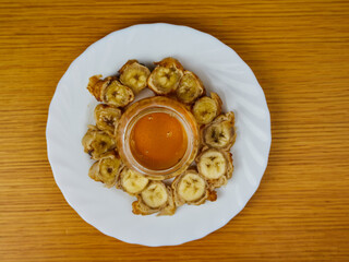 Delicious Fried slices of the ripe plantain and a glass of honey making a beehive on a round wooden plate. Top View