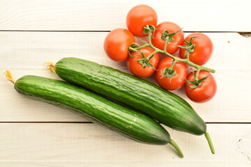 Several green cucumbers and red ripe, cocktail tomatoes on a twig, close-up, on a wooden table, top view.