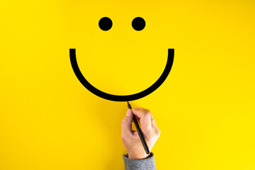 Male hand drawing a smiling happy face sketch on yellow background. Client satisfaction.