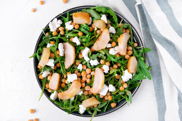 Salad with chickpea, arugula, caramelized pear, feta cheese served on the ceramic plate on the white table