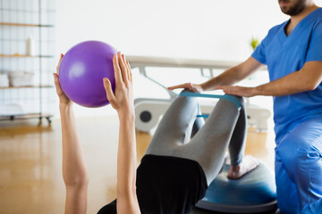 Detail of woman's hands holding purple fitness ball during recovery session in a medical center or...