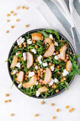 Salad with chickpea, arugula, caramelized pear, feta cheese served on the ceramic plate on the white table