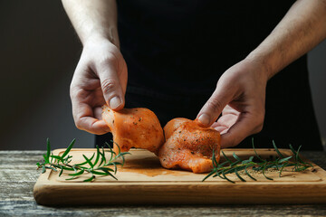 Chef cooking chicken fillet with herbs and spices on wooden board. Preparing fresh chiken meat. Healthy homemade food.