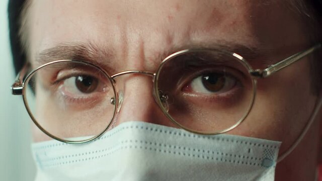 Close-up face of young man in protective mask, wearing glasses, hat. Headshot of funny hippster. Looking at the camera. Portrait of brown-eyed serious student. 