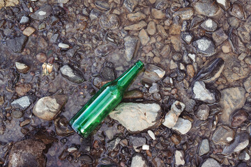 Glass bottle at river coast, top view. Water pollution concept. Contamination of the environment by humans.