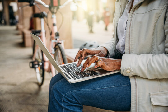 Young woman works at laptop sitting on a bench to send urgent work on the way to home with her bicycle after a day of work - Unrecognizable person - Concept of outdoor work