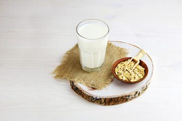 Oatmeal milk in a glass, oatmeal in a ceramic bowl on a white wooden background. Vegetable milk.
