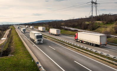 Convoys or caravans of transportation trucks passing on a highway on a bright blue day. Highway transportation with white and red lorry trucks