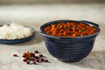RAJMA CURRY KEPT IN A BOWL ALONG WITH RICE AND RAW BEANS	
