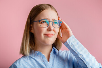 Woman is suffering from stress headache. Sad upset Emotional portrait office worker or student in glasses sick with migraine and holds temple with hand isolated over pink color background.