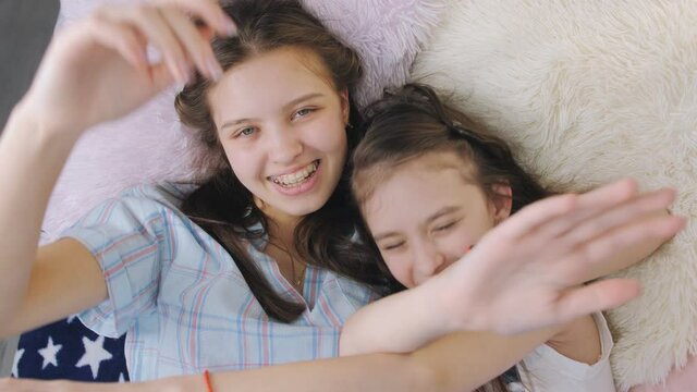 A carefree time at home. Two teenage sisters lie on the bed looking at the camera smiling and hugging.