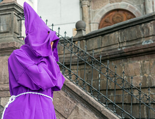 Portrait of a covered Cucurucho penitent with purple cape during the Easter procession in front of the San Francisco convent in Quito, Ecuador. 