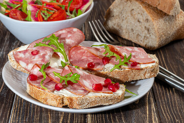 Smoked sausage and cream cheese sandwiches on a plate. Decorated with dill herbs. On a dark wooden background.
