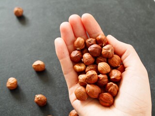 Female hand with hazelnuts on black background with place for text. Healthy food, snacks and lifestyle. Healthy breakfast. Woman holding nuts