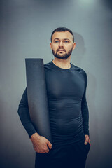 Handsome fitness man carrying an exercise mat and ready for his yoga class on a grey background