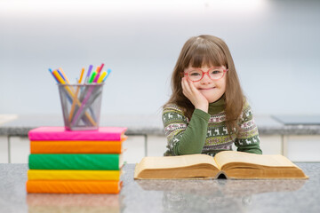 A girl with down syndrome reading a book at home and smiling while looking at the camera. Family education for children with disabilities