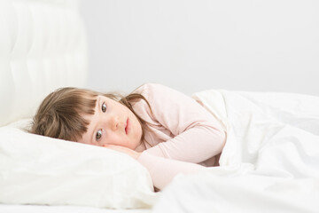 A girl with down syndrome lying on the bed under the covers and getting ready for bed. Usually childhood in a family for children with disabilities