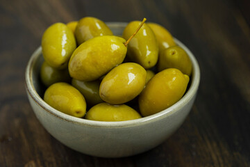 Green marinated olives in a bowl,
 horizontal background macro shot. Beautiful organic olives on dark wooden table, close up textured view, copy space.