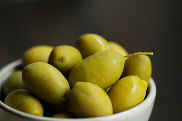 Green marinated olives in a bowl,
 horizontal background macro shot. Beautiful organic olives on dark wooden table, close up textured view, copy space.