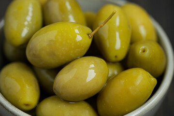 Green marinated olives in a bowl,
 horizontal background macro shot. Beautiful organic olives on dark wooden table, close up textured view, copy space.