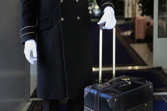 The doorman is holding a suitcase. Uniform and white gloves on the doorman.An unrecognizable person. Free space.Concept of hotel service