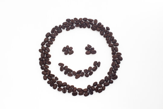 Roasted coffee beans arranged in a smiling face on a white background.