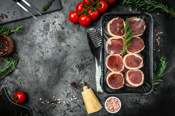 Raw pork medallion steaks wrapped in bacon served in packed on dark concrete background with spices salt and pepper. top view