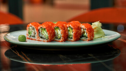 Closeup shot of set of red sushi rolls with caviar, seafood, wasabi and ginger laid out on a white plate on a table of Japanese restaurant