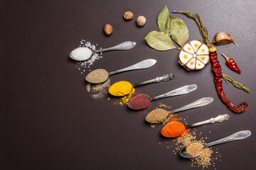 Assorted spices in spoons, herbs and vegetables on black stone background