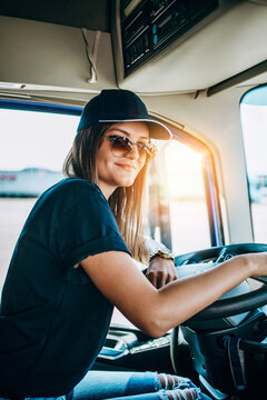 Portrait of beautiful young woman professional truck driver sitting and driving big truck. Inside of vehicle. People and transportation concept.