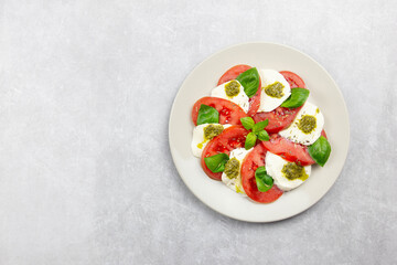 Traditional italian caprese salad with sliced tomatoes, mozzarella, basil, pesto sauce and spice on a light background. Top view. Copy space.