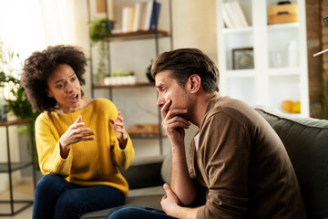 Frustrated young couple arguing at home. Stressed unhappy wife and husband sitting on cauch at home.