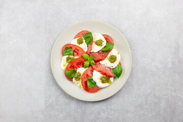 Traditional italian caprese salad with sliced tomatoes, mozzarella, basil, pesto sauce and spice on a light background. Top view.