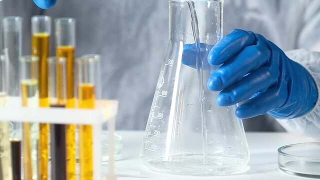 Chemist ia protective suit and gloves in modern lab pours clear solution into large glass tube. Laboratory research and pharmaceutical technologies. Research biological in the pharmacological industry