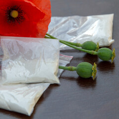 drug production concept: flowers and opium poppy heads next to packages of heroin, soft focus,...