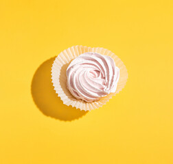 On a yellow background lies a pink marshmallow with a hard shadow. Blank for the pattern. Selective focus.