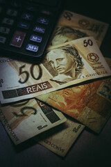 Bill of 50 Brazilian Real with a calculator and other bills under them